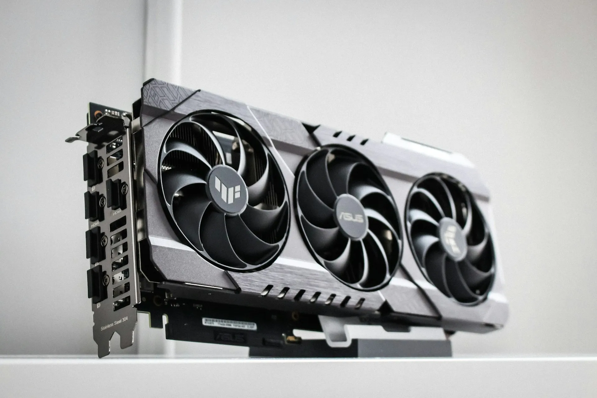 An ASUS TUF graphics card with three fans, standing on a white shelf